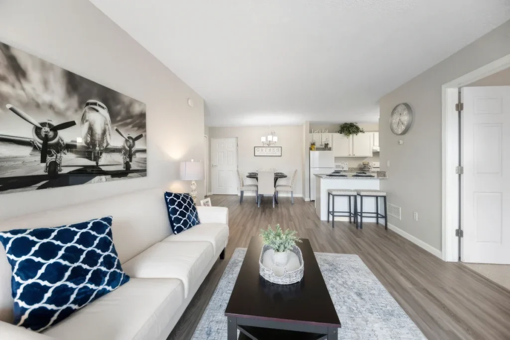 Living room with a white sofa, blue patterned pillows and black-and-white airplane wall art, with an open kitchen beyond