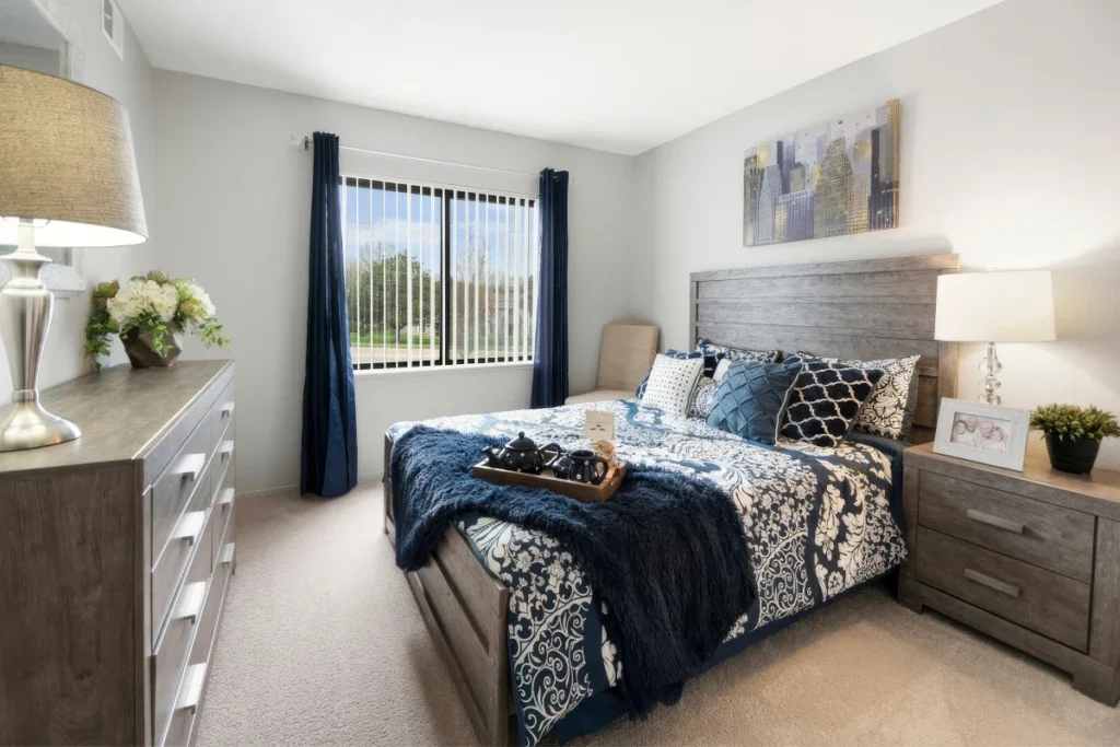 Bedroom with a gray headboard, navy and patterned bedding, a dresser and a window with navy curtains