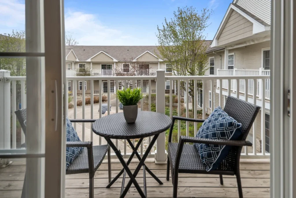 Balcony with a small round table and two cushioned chairs overlooking trees and neighboring buildings