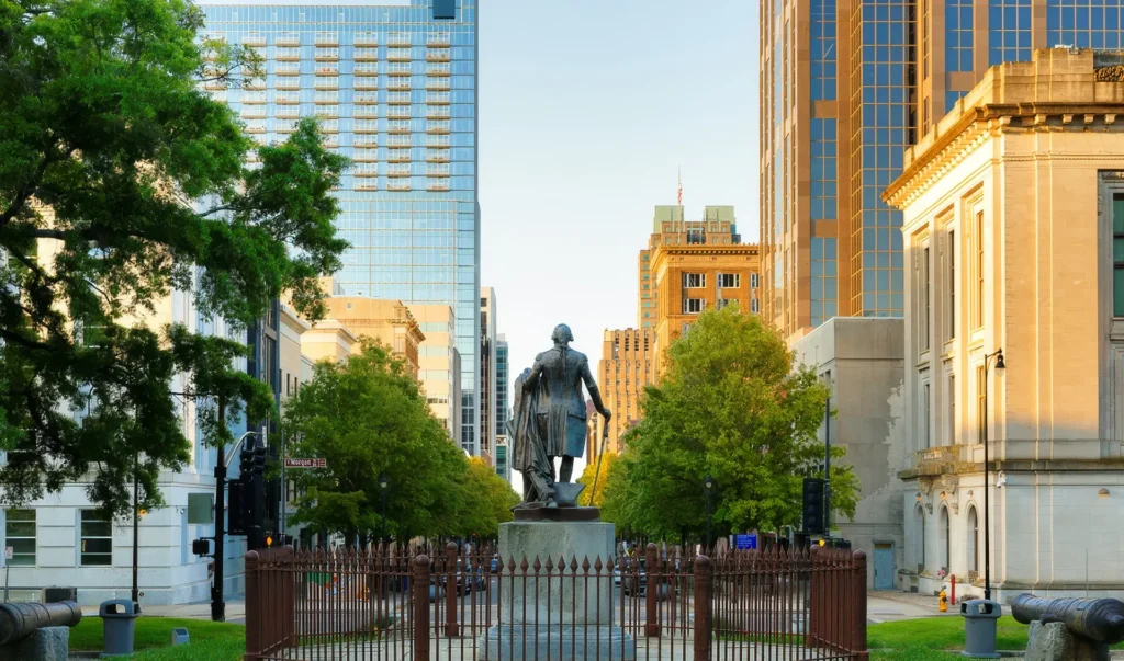 Downtown plaza with a statue framed by tall buildings and trees