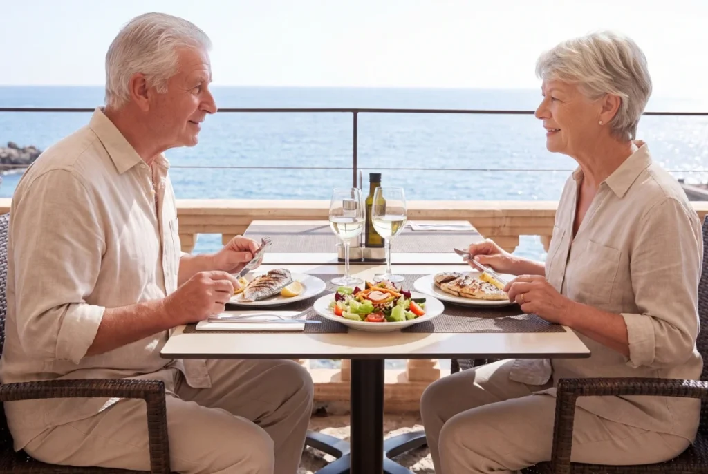 Older couple sharing a meal at a table on a balcony overlooking the sea