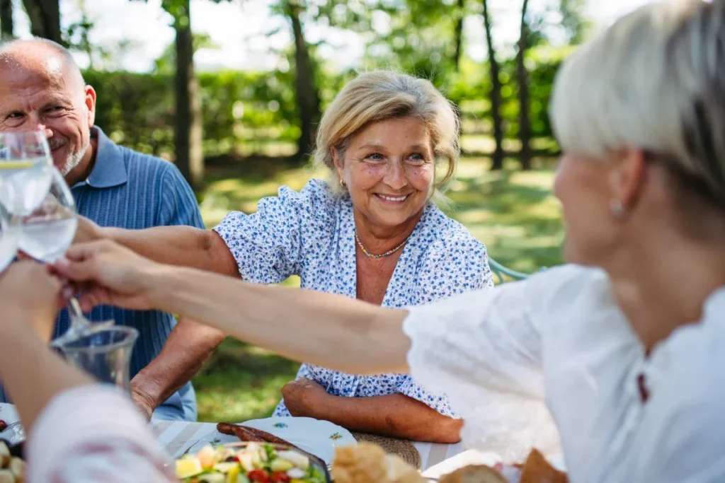 Older adults toasting with glasses at an outdoor picnic table