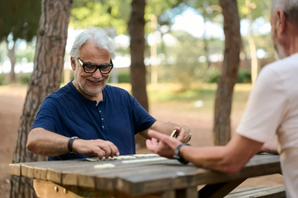 Older man smiling as he plays a game with another person at an outdoor picnic table
