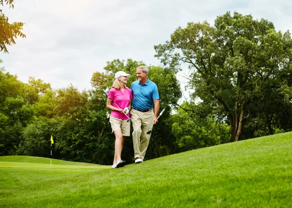 Smiling older couple in golf attire walking together on a grassy golf course