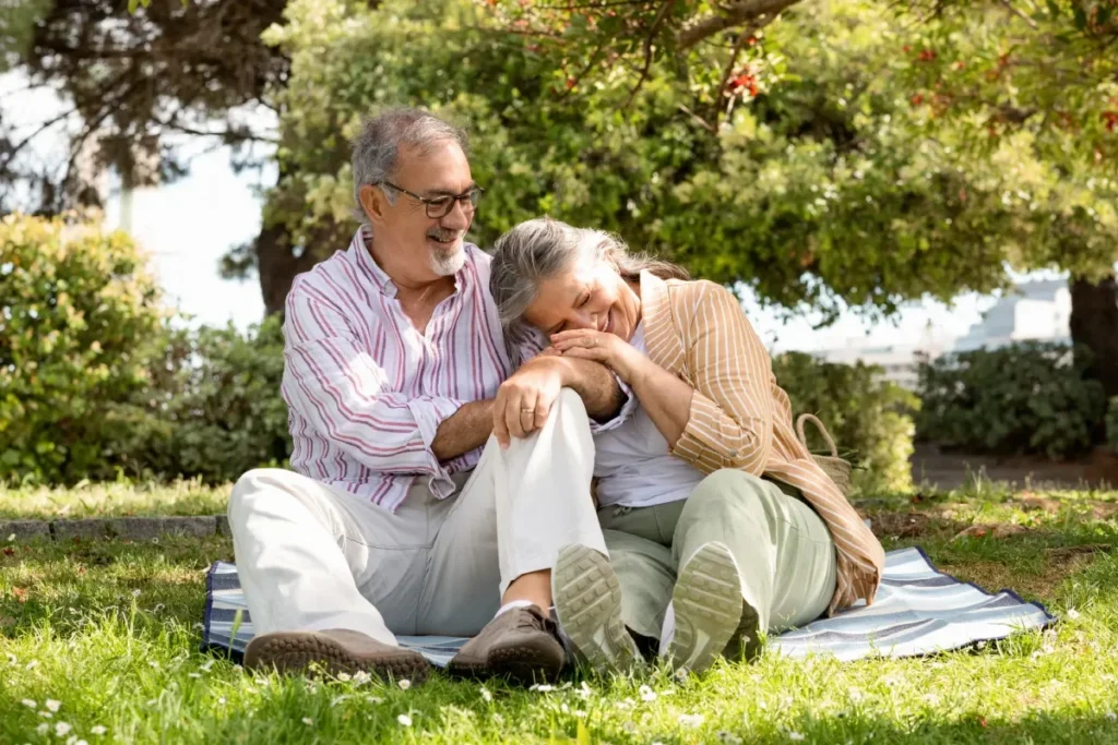 Older couple sitting close together on a blanket on the grass under a tree
