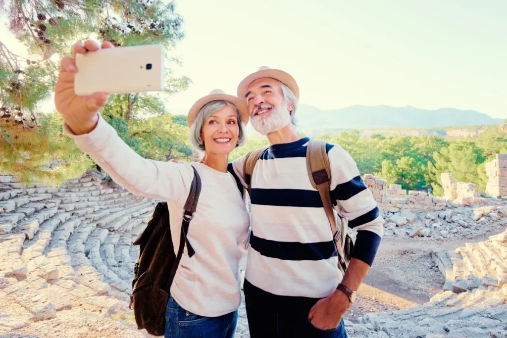 Smiling older couple in hats and backpacks taking a selfie on stone steps outdoors