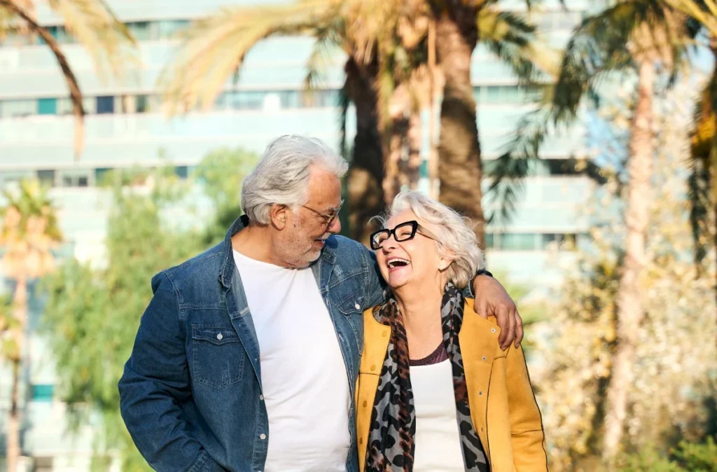 Smiling older couple laughing together outdoors, the man with his arm around the woman's shoulders