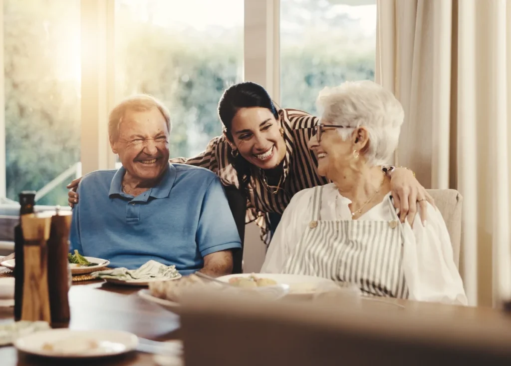 Older couple smiling with a younger woman who leans in between them at a table