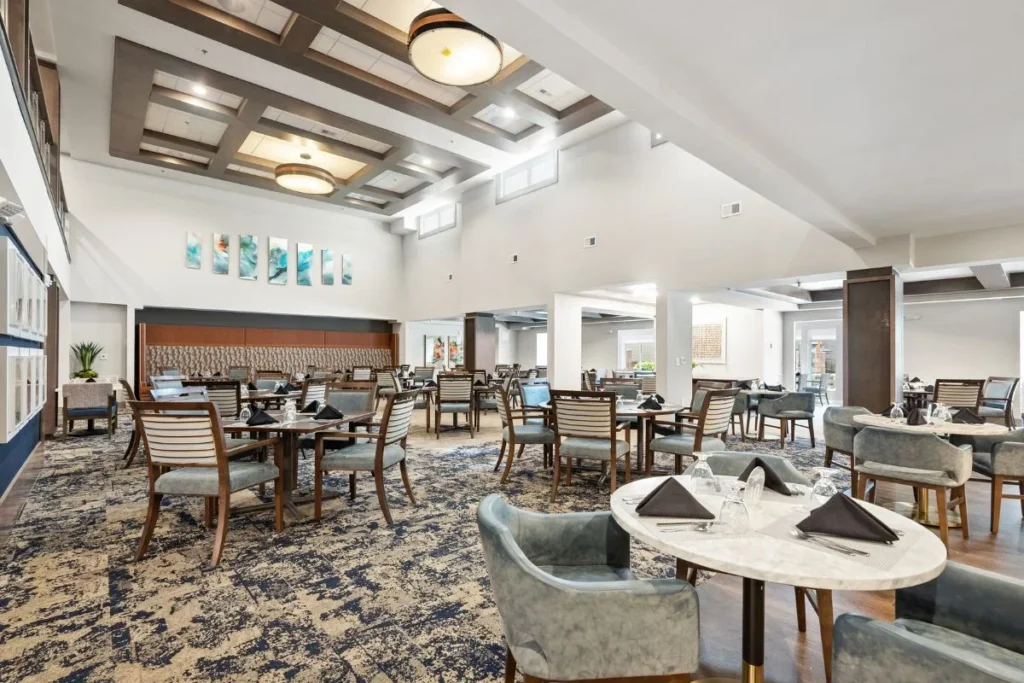 Dining hall with round tables set with napkins, cushioned chairs and a high ceiling with wood-beam accents