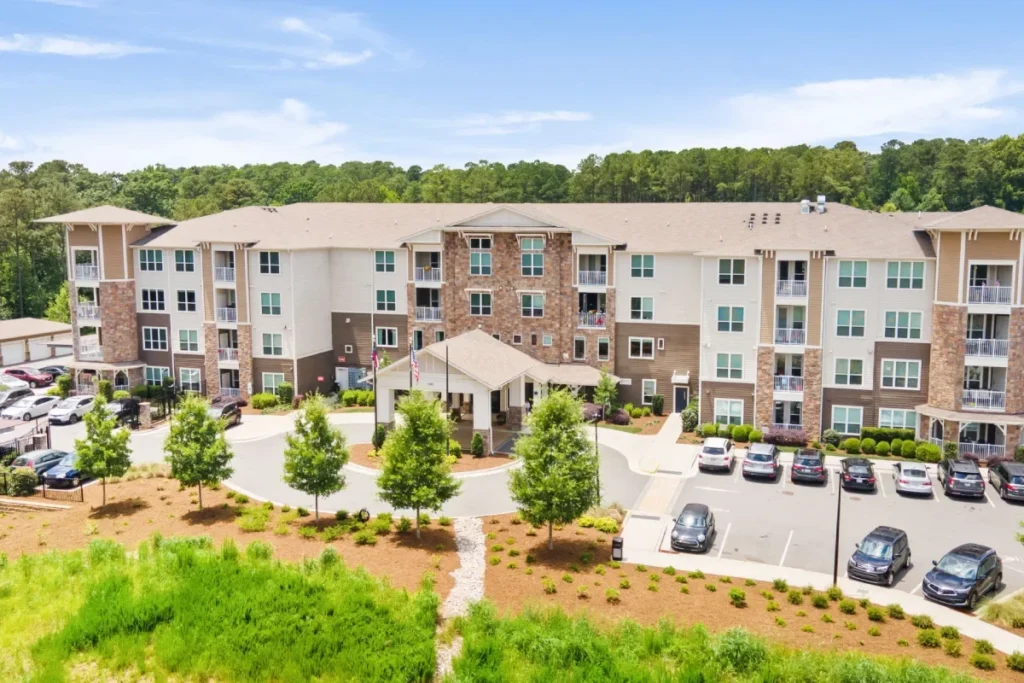Elevated view of an apartment building with a parking lot, surrounded by trees and green lawn