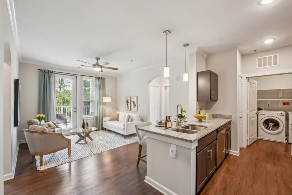 Open apartment kitchen with an island and pendant lights, a living area and a laundry closet