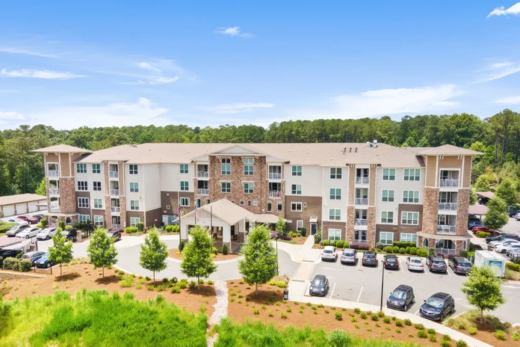 Elevated view of a four-story apartment building with a parking area, surrounded by trees and lawn