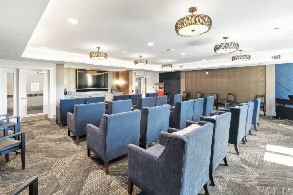 Media room with rows of blue armchairs facing a screen, under a tray ceiling