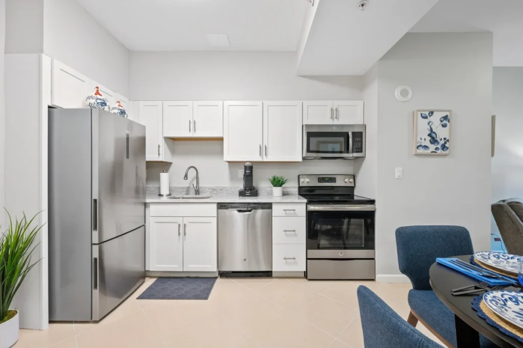Kitchen with white cabinets and stainless steel appliances beside a living area with blue armchairs