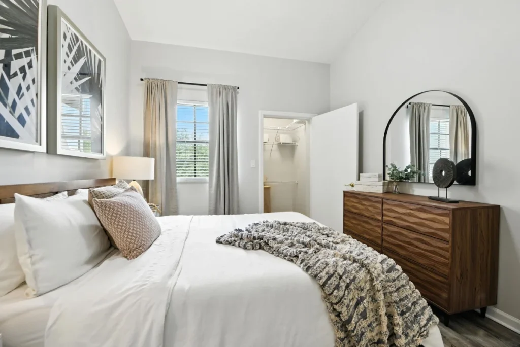 Bedroom with a white bed, a wooden dresser, an arched mirror and botanical wall art