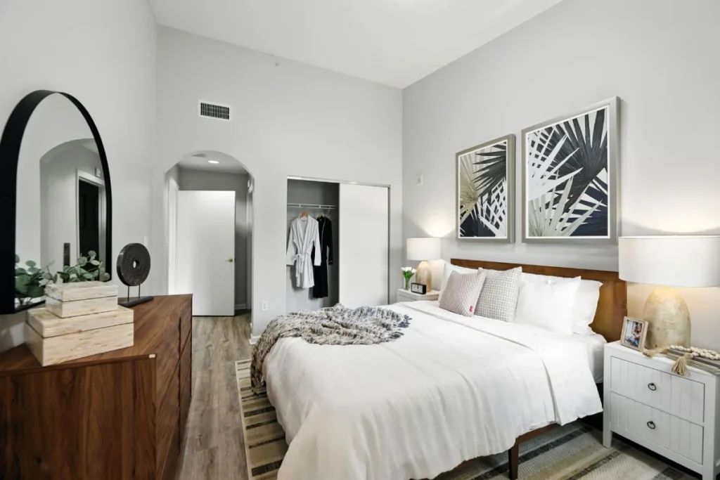Bedroom with a white bed, a wooden dresser with an arched mirror and leaf-print art above the bed