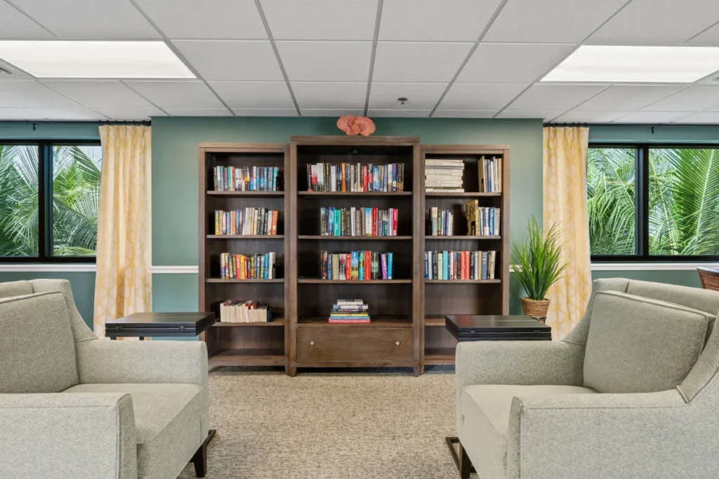 Library nook with a wooden bookcase full of books between cushioned armchairs and windows