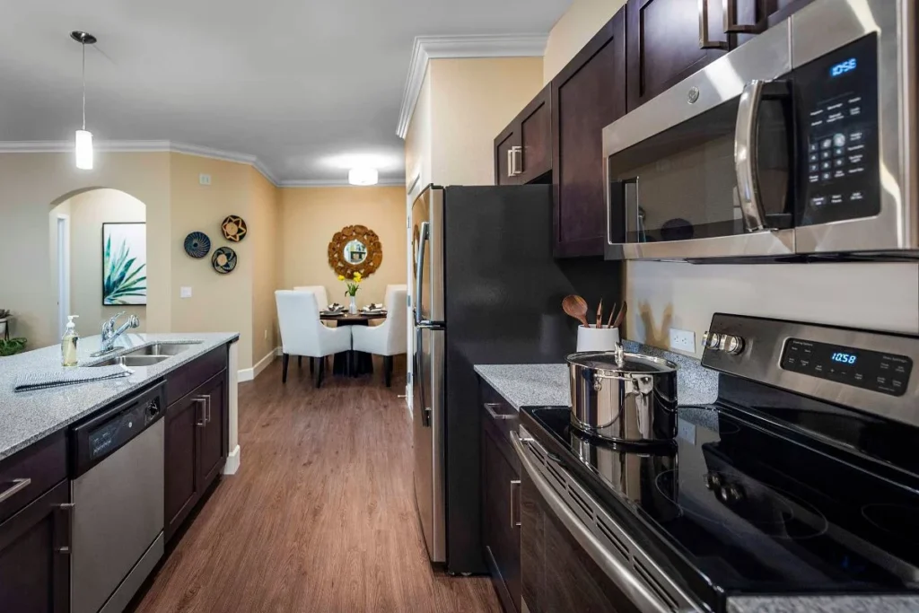 Kitchen with dark cabinets and stainless steel appliances, with a dining table beyond
