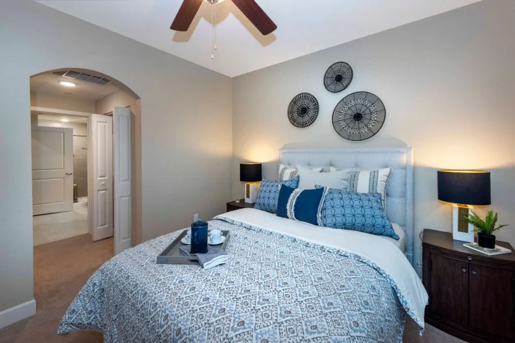Bedroom with a bed in blue patterned bedding, dark lamps on the nightstands and round wall decor