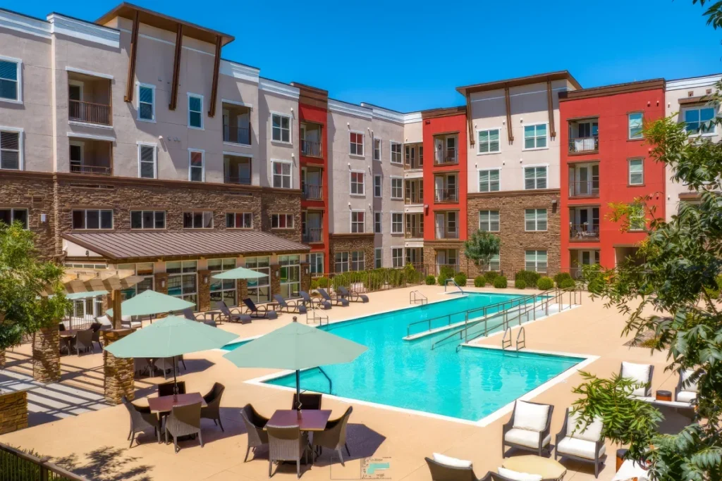 Courtyard swimming pool with lounge chairs and teal umbrellas, surrounded by multi-story apartment buildings