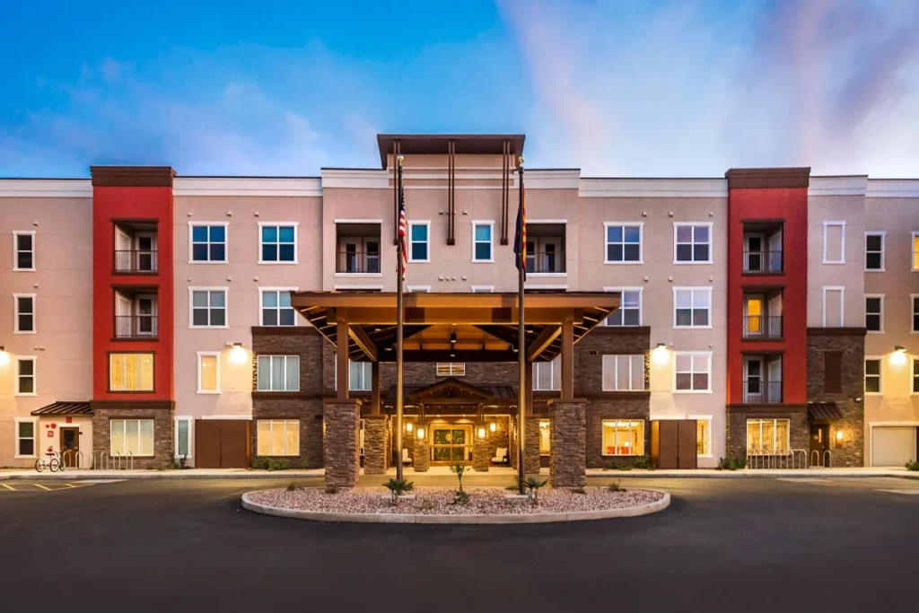 Front entrance of a multi-story apartment building with red and pink accents, lit at dusk