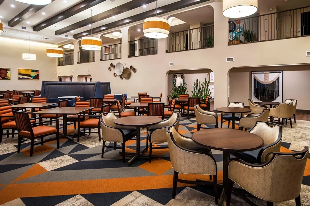 Spacious dining area with round tables, cushioned chairs and pendant lights, with a balcony level above