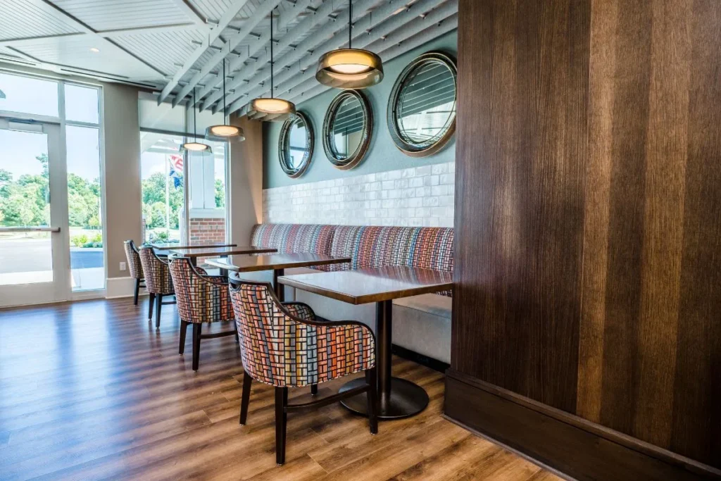 Café-style dining area with booth seating, patterned chairs and round mirrors beside large windows