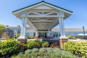 Covered entrance with white columns and brick bases at the front of a modern building, framed by flowering shrubs