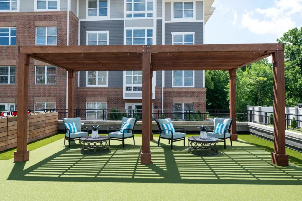 Rooftop patio with a wooden pergola, lounge chairs and artificial turf beside a brick building