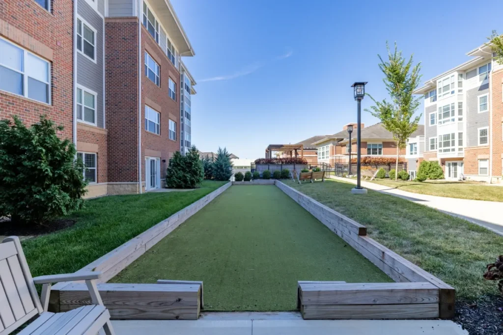 Narrow lawn strip bordered by wooden planters and benches, running through a courtyard of brick apartment buildings