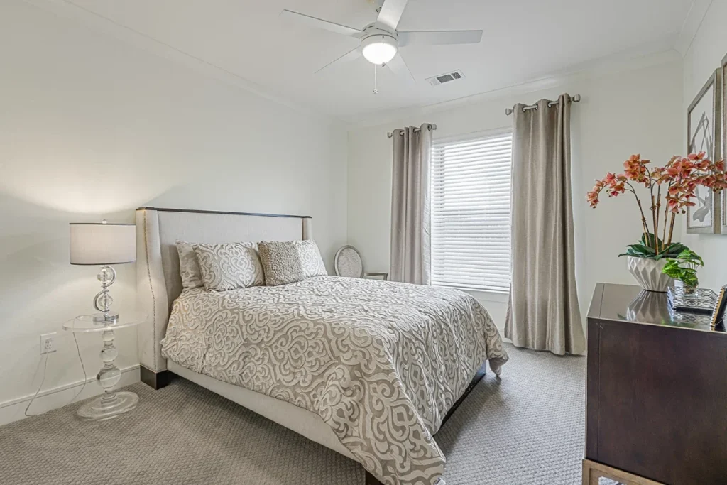 Bedroom with a patterned bedspread, a table lamp, a ceiling fan and an orchid on the dresser