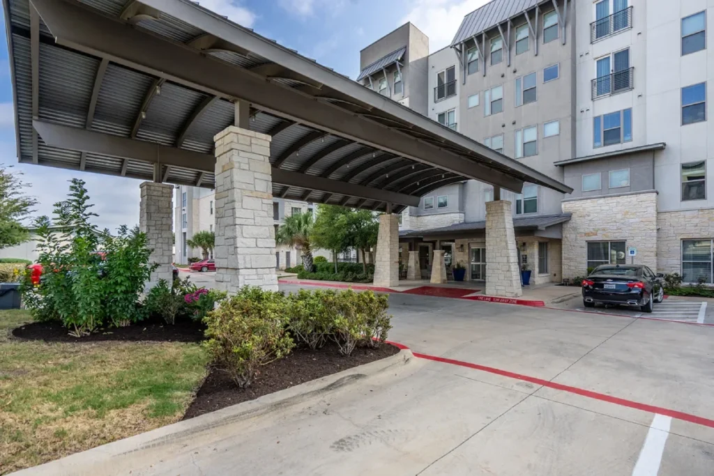Covered drive-up entrance with a stone column beside a multi-story building and parking