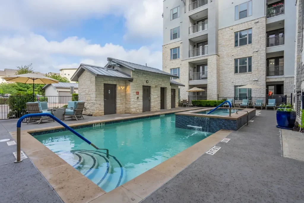 Courtyard pool with steps and a small pool house, with a multi-story building behind