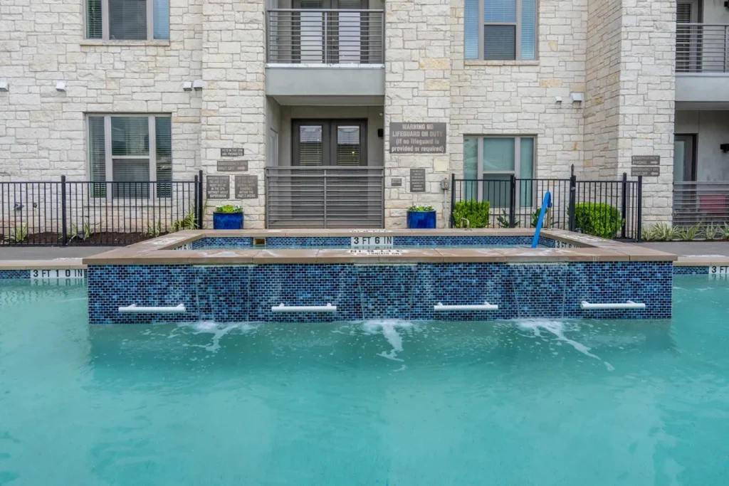 Swimming pool with a blue-tiled raised spa in front of a multi-story stone building