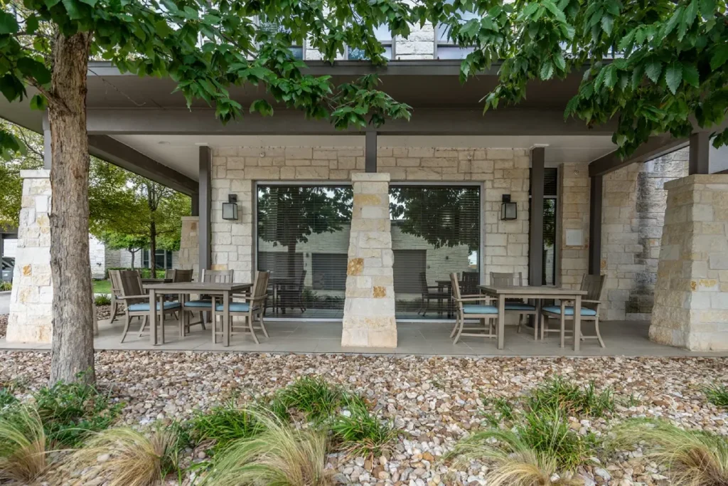 Covered stone patio with tables and chairs under shade trees