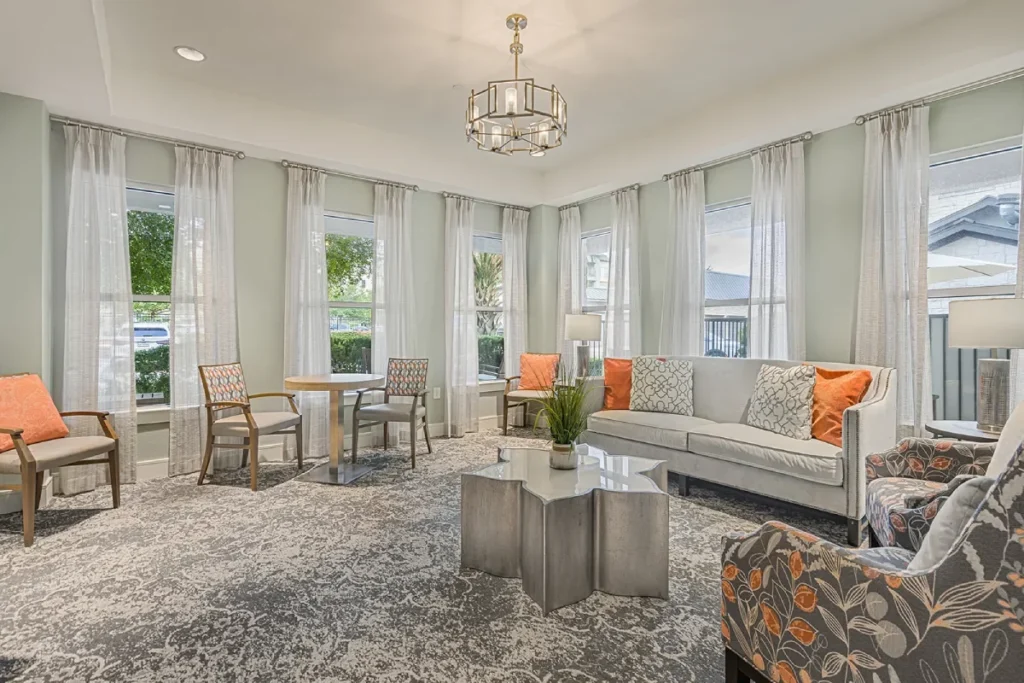 Bright lounge with a light sofa, orange accent chairs, a coffee table and a chandelier