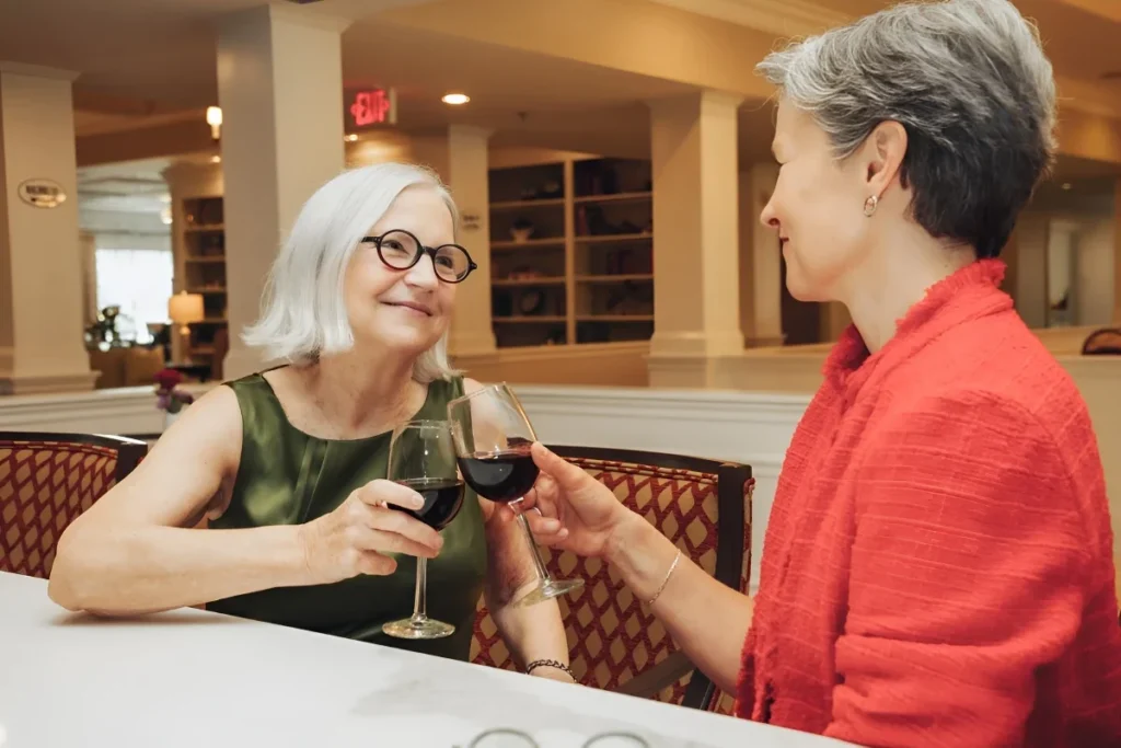 Two senior women chatting over glasses of red wine at a table
