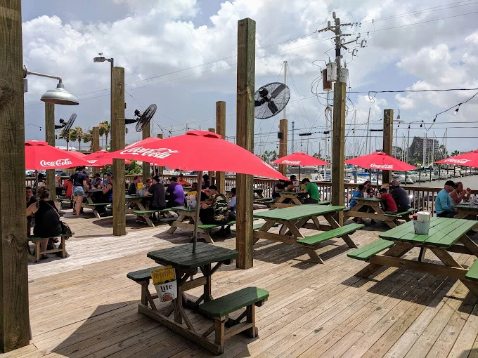 Outdoor deck with picnic tables and red umbrellas at a waterfront restaurant