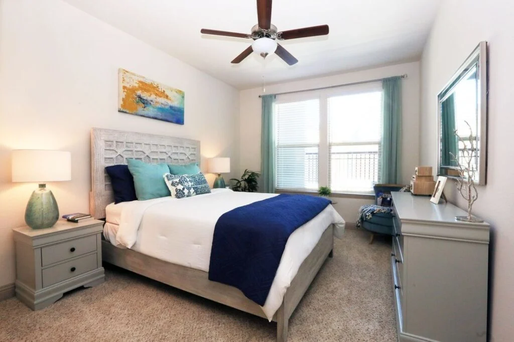 Bedroom with a made bed, ceiling fan and large windows