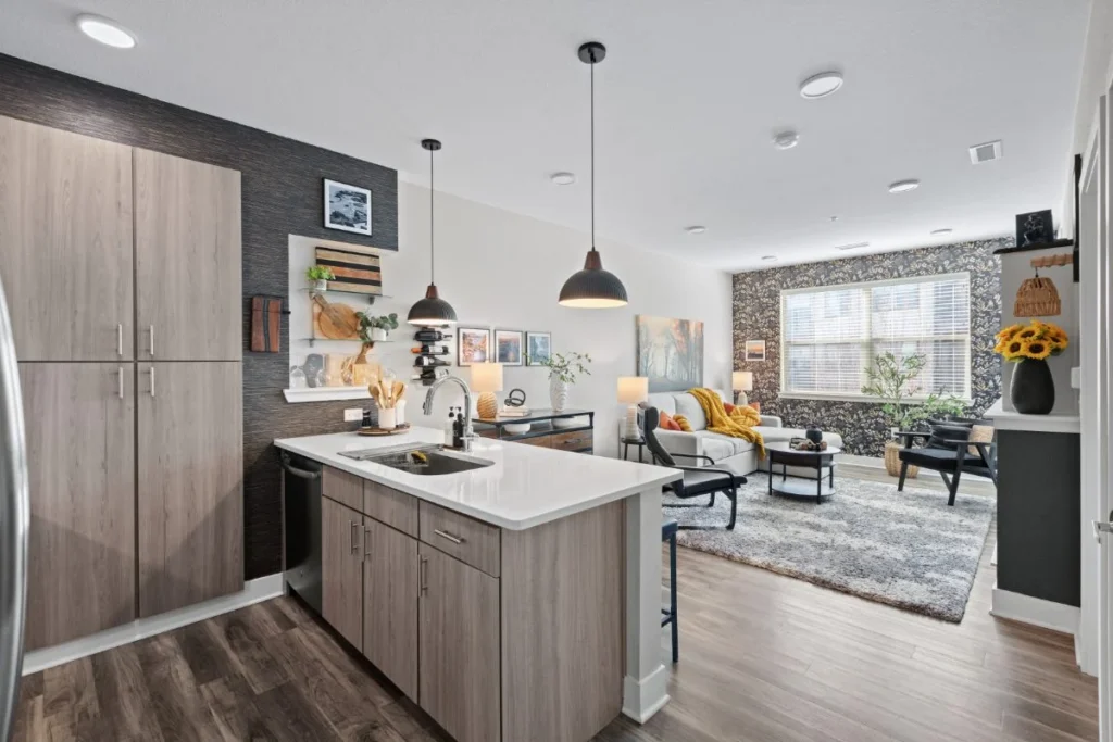 Kitchen with light wood cabinets and an island with pendant lights, opening to the living area