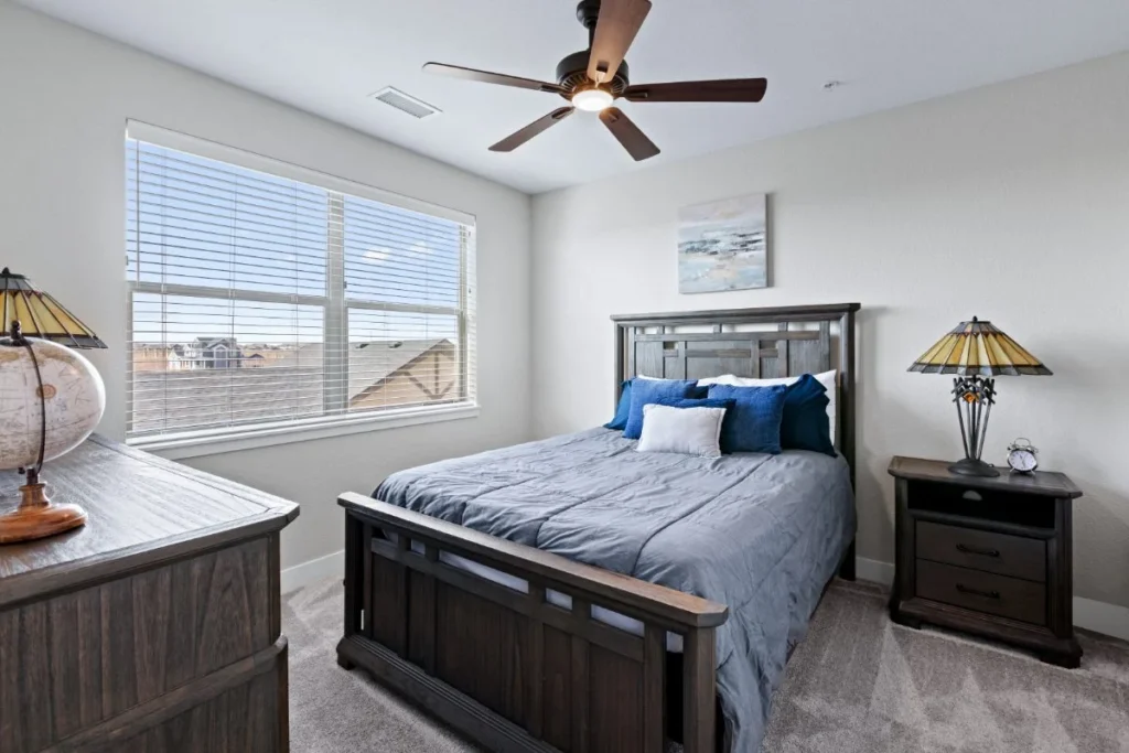 Bedroom with a wooden bed frame, blue bedding, a ceiling fan and nightstand lamps