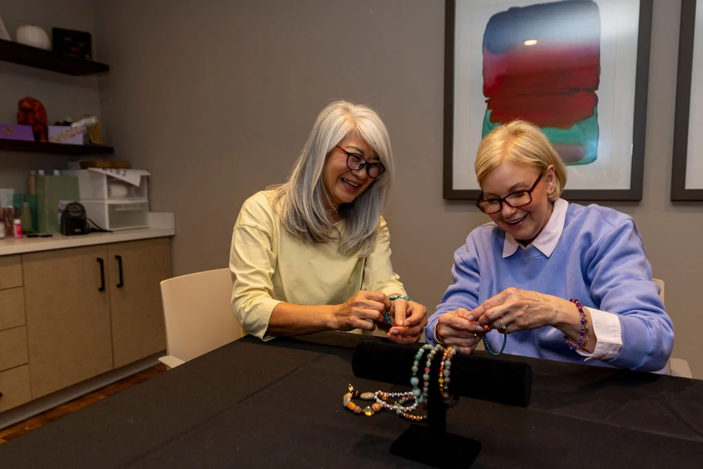 Two senior women making beaded jewelry at a table