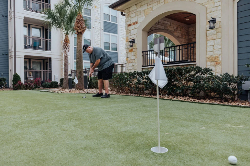 Senior man practicing on a putting green outside an apartment building