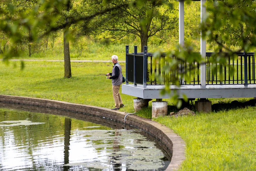 Senior man standing near a pond and covered gazebo in a park