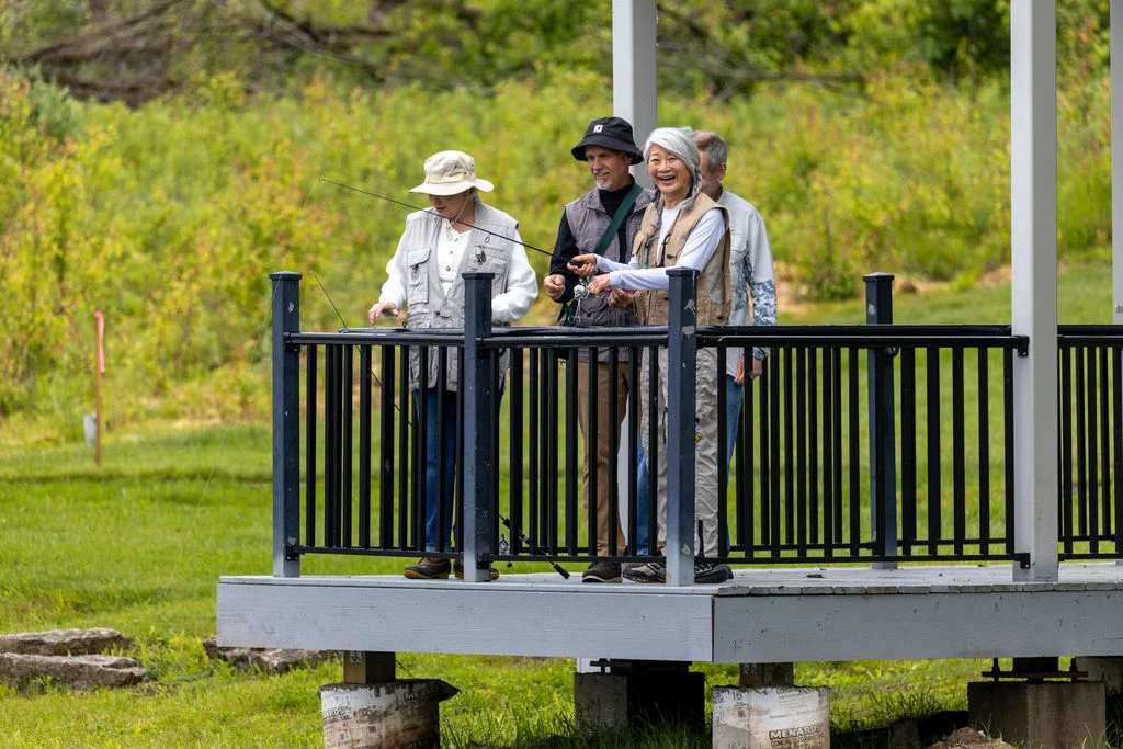 Three seniors in sun hats standing on a covered observation deck overlooking a green field