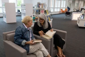 Two senior women reading together in a library lounge