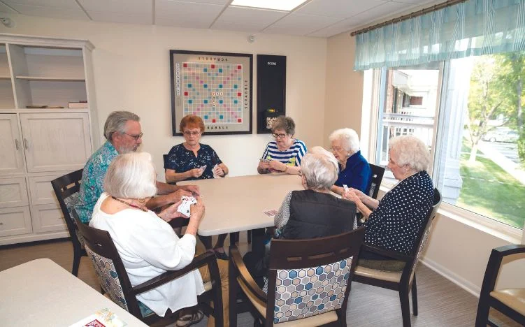 Residents gathered around a table playing cards in a bright community room