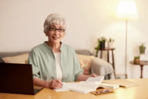 Senior woman with glasses writing in a journal while seated on a couch