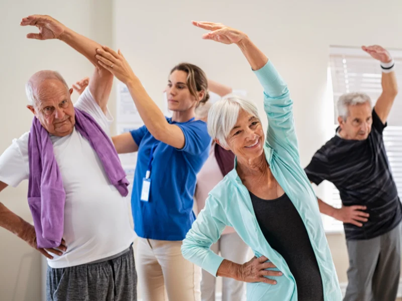 Group of seniors doing a standing stretch with a fitness instructor